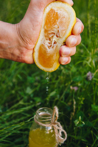 在户外的草地上,男性用手将柑橘类水果汁挤到一瓶自制的柠檬水里.