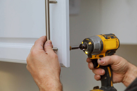 安装工人用螺丝刀把白色的柜子拿起来照片