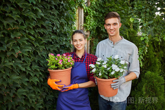 在一个阳光明媚的日子里在美丽的花园里微笑的男女园丁手拿花盆手拿
