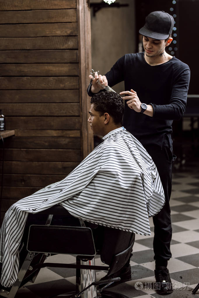 一位穿着黑色衣服的理发师剪着坐在镜子对面的扶手椅上的男人的头发
