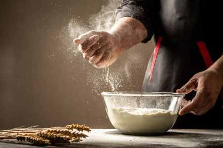 打面粉白色的面粉飞向空中,身着黑色西装的糕点厨师正在用力打圆球.