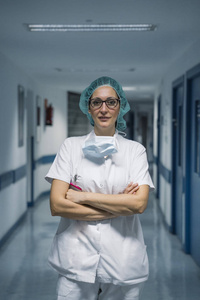 外科手术帽女医生穿着制服,戴着口罩,戴着医疗帽,双手交叉在医院走廊