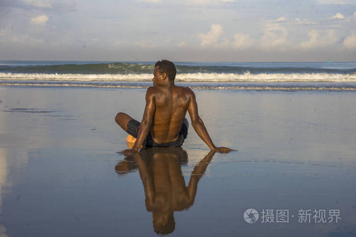 年轻迷人放松的黑人美国黑人男子，身体健康，背部肌肉发达，坐在沙滩上欣赏美丽的景色，自由思考和冥想