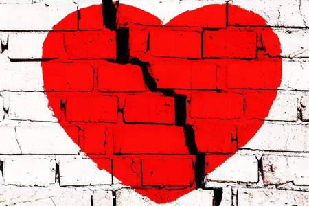 在砖墙上的心红色破碎的心在砖墙上,中间有大裂缝.破碎爱情的概念照片