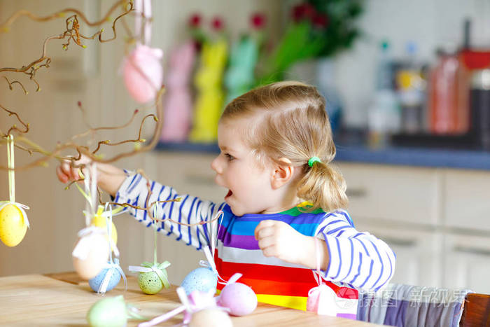 可爱的蹒跚学步的小女孩用彩色彩色塑料蛋装饰树枝。快乐的小宝宝玩复活节装饰品玩得开心。可爱健康的微笑孩子享受家庭假期