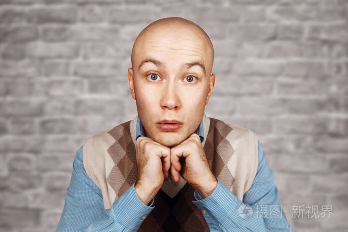 白砖墙背景上的一个光头男人的画像一只手穿着蓝色衬衫
