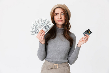 困惑的美女拿着钱和信用卡孤立在白色的墙背景上.照片