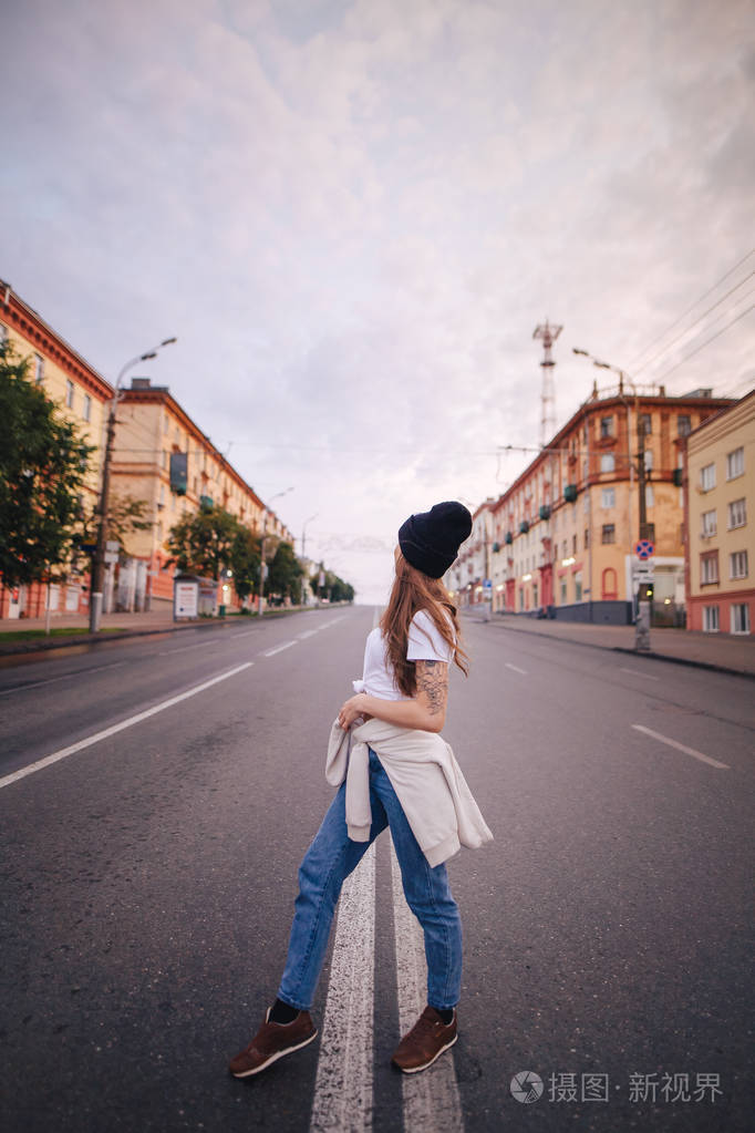 在马路中间摆姿势的女孩穿着时髦衣服戴着帽子的女孩