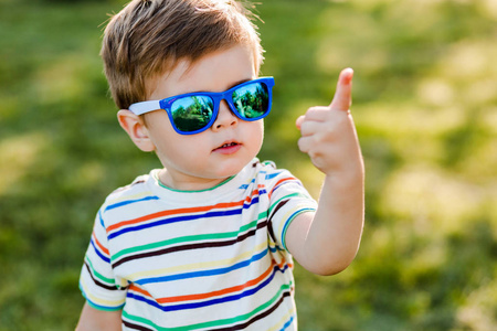 不戴墨镜的小马哥戴着明亮墨镜的可爱小男孩展示了夏日花园的第一名.