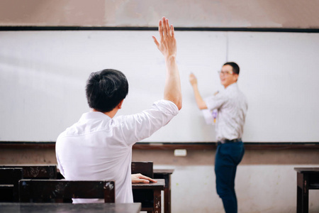 年轻的成年男学生举起手向另一位男老师提问.照片
