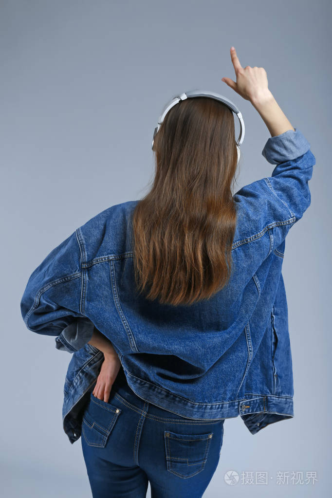 戴着耳机的年轻女子在灰色背景下听音乐