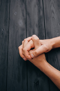 双手交叉的手指,白色的男性双手交叉在黑色乡村木桌子上.俯视图.