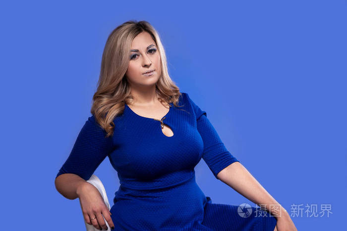 在蓝色背景的工作室里,一个有着巨大乳房的曲线金发模特照片-正版商用