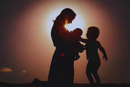 夕阳下幸福的母亲带着刚出生的婴儿和小女儿照片