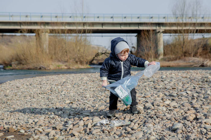 节约环保理念一个小男孩在海滩上收集垃圾和塑料瓶扔进垃圾桶