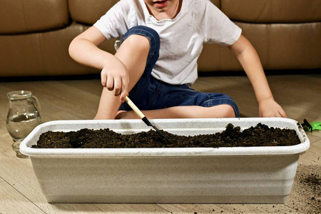 用铲子在地上一个男孩用铲子在地上挖土,坐在他前面的地板上.照片