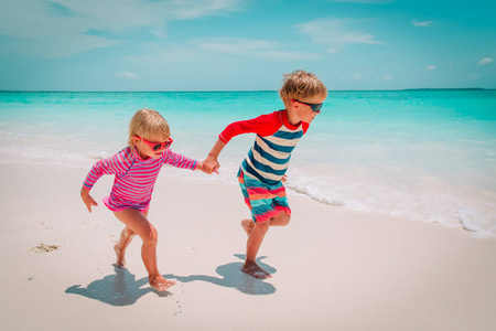 小男孩和女孩在海滩上跑步,孩子们在假期里玩耍照片