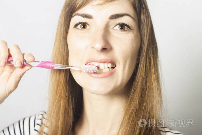 一个年轻女孩在浅色的背景上刷牙口腔护理概念个人卫生牙科