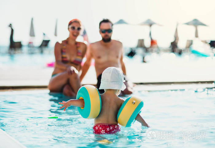 暑假时，一个戴着臂章的小孩和父母在游泳池里。