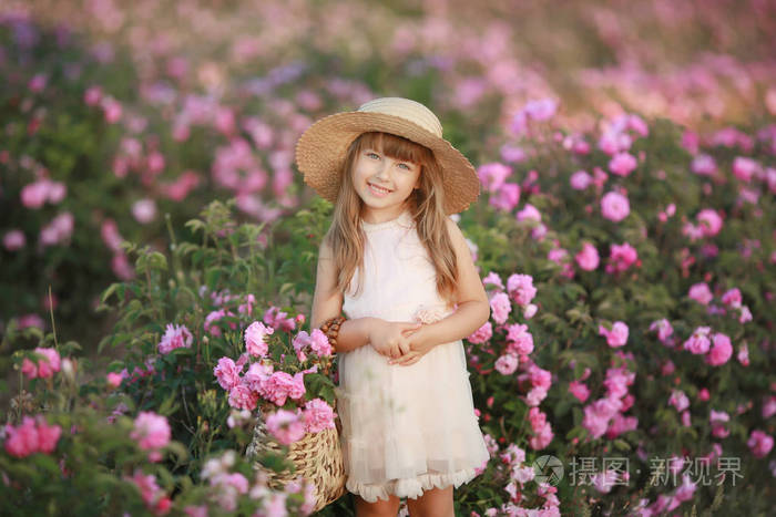 一个金发碧眼的小女孩，穿着一件浅色的连衣裙，头上戴着一圈真正的花，在一朵茶玫瑰的花园里