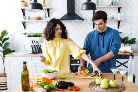 年轻可爱的微笑情侣在家里的厨房里一起做饭.