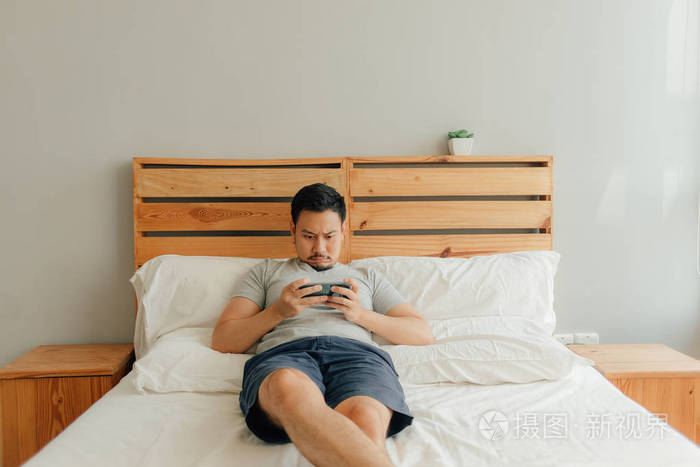 男人在床上用智能手机玩手机游戏