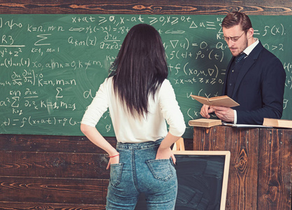 一个黑发女学生站在老师面前,手放在牛仔裤后面的口袋里照片