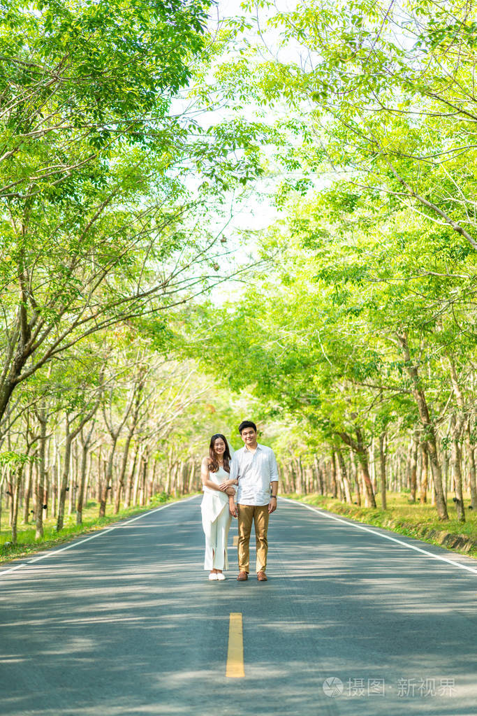 幸福的亚洲情侣在树拱门的路上相爱