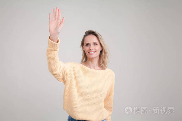 漂亮的女学生打招呼微笑愉快友好挥舞着她的手灰色背景下的姿势表情