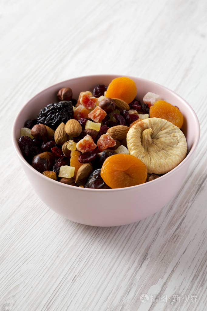 干果和坚果放在白色木质背景的粉红色碗里