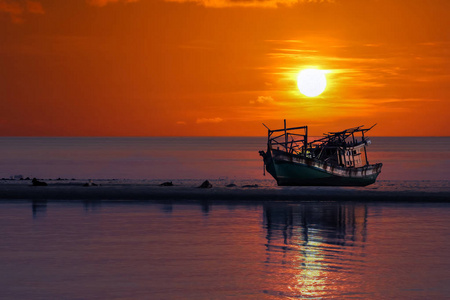 夕阳下,红色的天空,沙滩上遗弃了一条破船照片