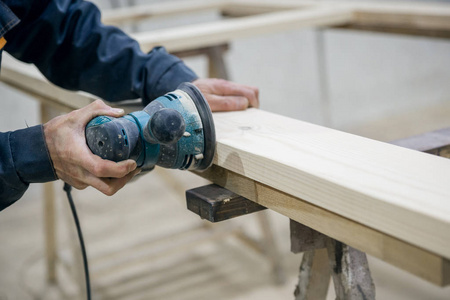 工人用砂纸打磨木头表面.在电动工具的手中.照片