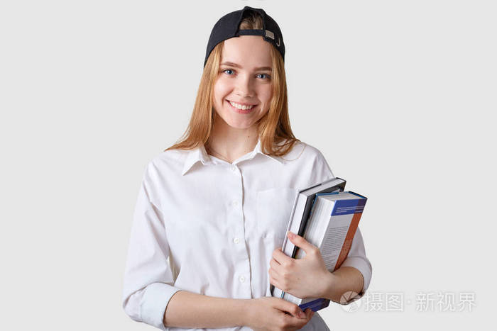 年轻的微笑着的学生拿着一堆五颜六色的书在白色的背景下摆出姿势看