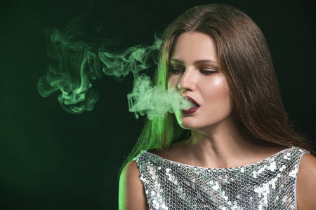 在黑暗背景下抽烟的年轻女子照片