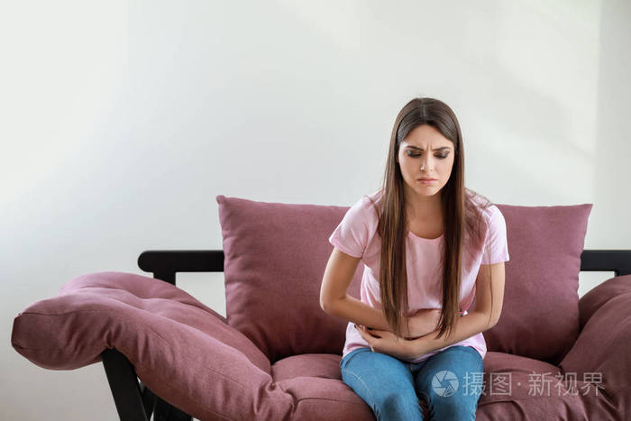 坐在白底沙发上腹痛的年轻女子