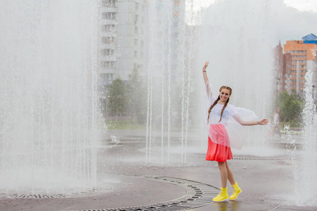 一个穿着黄靴子,梳着两条辫子的小女孩站在喷泉旁.照片