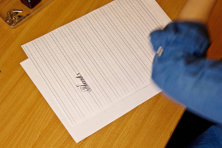 羽毛笔写字女性用墨水笔在有条纹的白纸上写字.