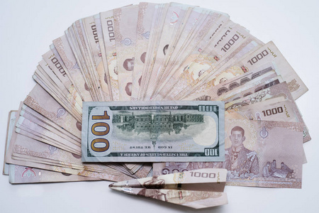 一堆泰铢和一百美元放在一张有飞机的白色桌子上.照片