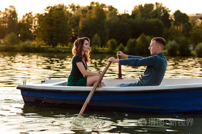 年轻的欧洲情侣在湖边划船年轻人和他的女朋友在日落时坐在船上相爱的