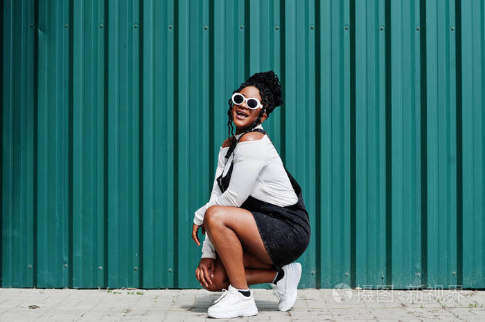 非洲女人穿着牛仔工装裤裙子戴着白色太阳镜蹲着