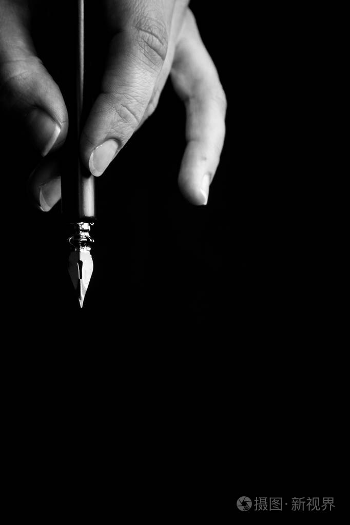 女性手优雅地拿着一支黑色背景上金属笔尖的钢笔经典钢笔孤立宏观黑白