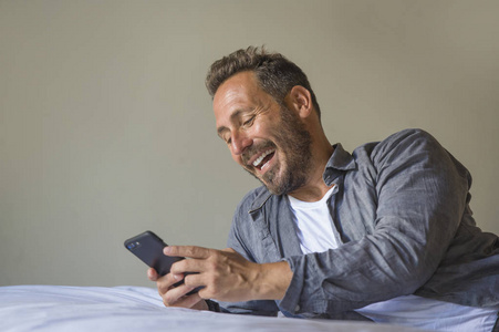 床网年轻帅气快乐的男人在家里用互联网手机在床上微笑开朗满足感轻松