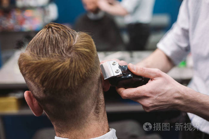 一名男子在理发店理发的特写镜头男发型师为客户服务使用机器和梳子