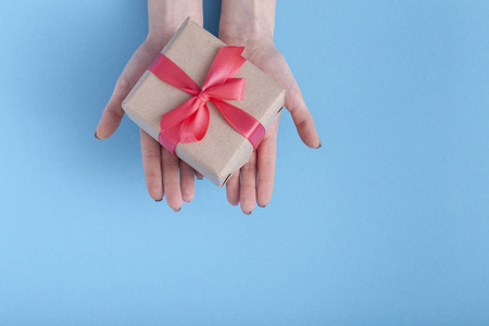 女孩在掌心向前伸展礼物,女士拿着礼盒,手上系着红色丝带蝴蝶结,背景