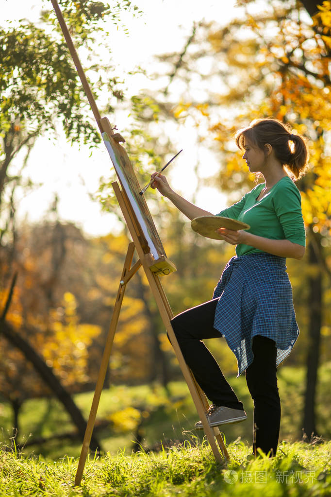 在大自然的画架上一个在画布上画画的女人一个拿着画笔和调色板的女孩