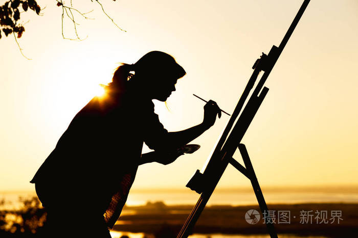 一个女人的剪影在画架上用画布上的颜料作画女孩拿着画笔和调色板在