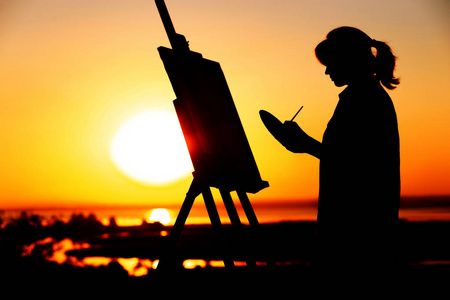 年毛笔一个年轻女子的剪影在自然的画架上画画,女孩的身影拿着毛笔和