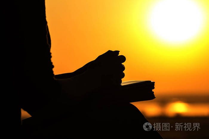 日落时的圣经中女性向上帝祈祷的手的剪影宗教和灵性的概念