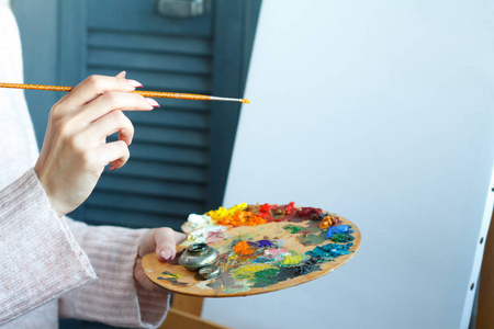 穿着粉色毛衣的女性手拿着刷子和彩色丙烯酸颜料的调色板照片