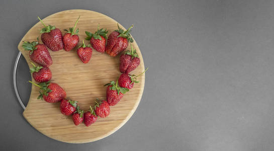 灰色纸背景上有红色草莓的圆形木制砧板.横幅,复制空间.从上面看.